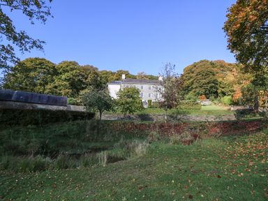 A large house surrounded by trees and grass with a stone wall and pond in the foreground at Llwynderw Hall in Abergwesyn near Llanwrtyd Wells