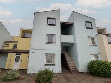 An exterior view of a multi-story residential building with stairs in the middle and bushes in front at Estuary Escape in Porthmadog
