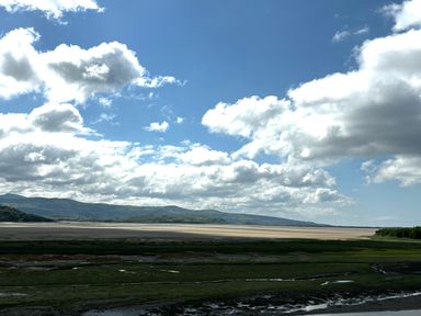 A coastal landscape with green marshland water channels and mountains under a cloudy sky at Estuary Escape in Porthmadog