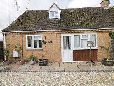 The exterior front view of a brick house with a mossy roof several potted plants a birdhouse white doors and windows at Ground Floor Annex in Milton-Under-Wychwood
