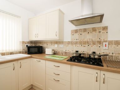A kitchen with cream cabinets a microwave a toaster a gas stove with pots and a tiled backsplash at Ground Floor Annex in Milton-Under-Wychwood