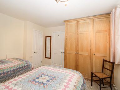 A bedroom with two beds covered by patchwork quilts a wooden wardrobe a wooden chair and two white doors at Ground Floor Annex in Milton-Under-Wychwood