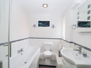 A bathroom with a bathtub a toilet a sink a mirror and wall decorations at Ground Floor Annex in Milton-Under-Wychwood
