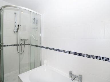 A bathroom with a glass shower enclosure and a bathtub with tiled walls at Ground Floor Annex in Milton-Under-Wychwood