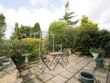 An outdoor patio area with a table and two chairs surrounded by plants and planters at Ground Floor Annex in Milton-Under-Wychwood