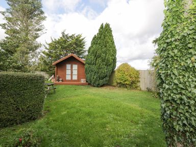 A garden with a wooden shed a picnic table and various trees and bushes at Ground Floor Annex in Milton-Under-Wychwood
