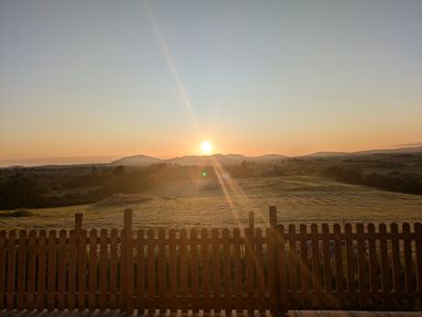 A sunset over hills and fields with a wooden fence in the foreground at Hafan Gelli Sheperds Hut - Tudwal in Pwllheli