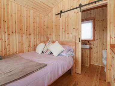 A bedroom with a wooden bed and multiple pillows and a sliding door leading to a bathroom at Hafan Gelli Sheperds Hut - Tudwal in Pwllheli