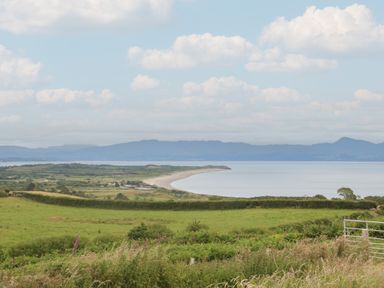 A coastal landscape with grassy fields and hills overlooking a curving beach and sea at Hafan Gelli Sheperds Hut - Tudwal in Pwllheli