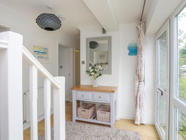 An entryway with a wooden table with drawers and baskets below a mirror a hanging light and a window with curtains at Mor Glas in Abersoch