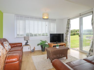 A living room with brown leather sofas a TV on a wooden stand and sliding glass doors opening to a garden at Mor Glas in Abersoch