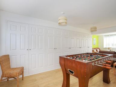 A room with a foosball table wooden chair white built-in cupboards and a seating area with a window at Mor Glas in Abersoch