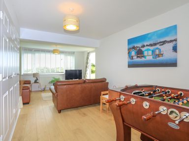 A living room with brown leather sofas a foosball table a television and a large window at Mor Glas in Abersoch