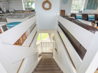 A staircase with carpet leading down between a kitchen counter with stools and a living room with a sofa at Mor Glas in Abersoch