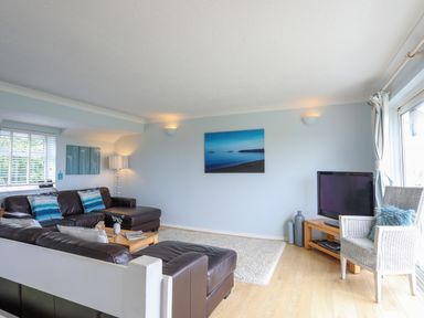 A living room with leather sofas a TV on a wooden stand a wicker chair and artwork on the wall at Mor Glas in Abersoch