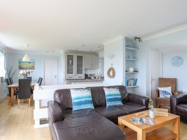 A living room with a leather sofa and a wooden coffee table next to a dining area with a wooden table and black chairs at Mor Glas in Abersoch