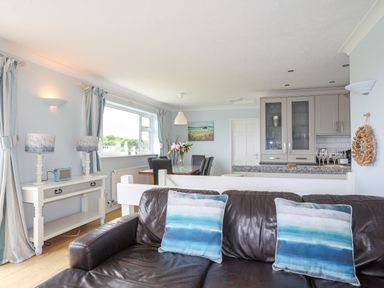 A living room with a brown leather sofa and blue cushions next to a dining area and a kitchen at Mor Glas in Abersoch