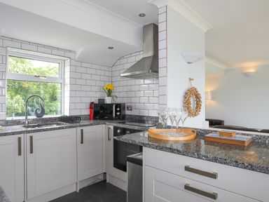 A kitchen with white cabinets granite countertops a window and stove at Mor Glas in Abersoch
