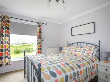 A bedroom with a patterned bedspread on a metal bed frame and a window with curtains at Mor Glas in Abersoch
