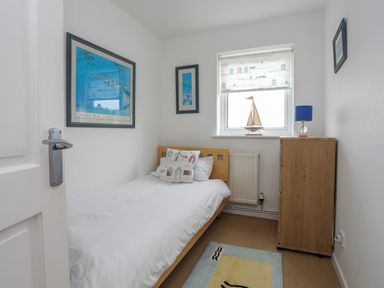 A small bedroom with a single bed wooden chest of drawers and a window at Mor Glas in Abersoch