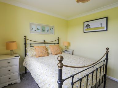 A bedroom with a metal bed frame two bedside tables with lamps and framed pictures on the walls at Mor Glas in Abersoch