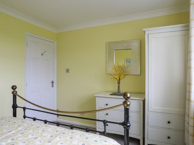 A bedroom with a white door a white dresser with a vase of yellow flowers a white wardrobe and a black metal bed frame at Mor Glas in Abersoch