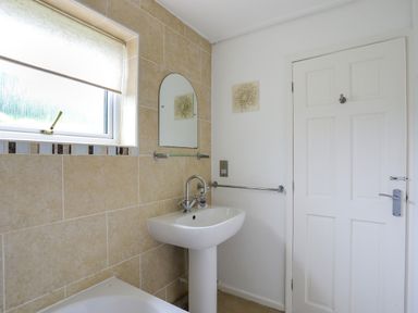 A bathroom with a white pedestal sink a mirror a wall-mounted towel rail and a window at Mor Glas in Abersoch