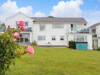 A white two-story house with balconies and a lawn with pink flowers in the foreground at Mor Glas in Abersoch
