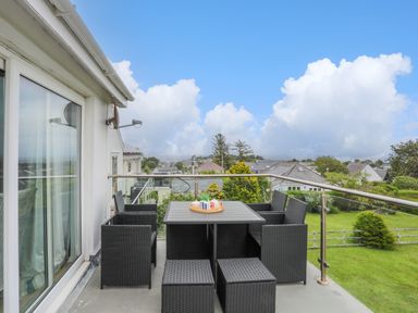 An outdoor balcony with a black table and chairs overlooking a green yard and rooftops at Mor Glas in Abersoch