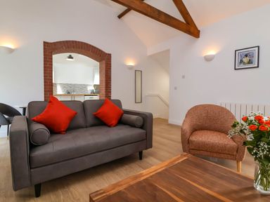 A living room with a gray sofa with red cushions an orange armchair a wooden coffee table and a view into a kitchen through a brick arch at Woodland Roost Parkham near Bideford