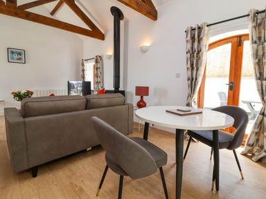 A living room with a sofa two chairs a round table a wood stove and wooden beams at Woodland Roost in Parkham near Bideford