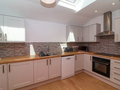 A kitchen with wooden countertops white cabinets a dishwasher an oven a stove a microwave a kettle and a toaster at Woodland Roost in Parkham near Bideford