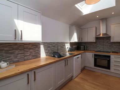 A kitchen with wooden countertops white cabinets a sink dishwasher oven stovetop microwave and kettle at Woodland Roost in Parkham near Bideford