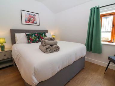 A bedroom with a bed with rolled towels bedside table lamps and a window with green curtains at Woodland Roost in Parkham near Bideford