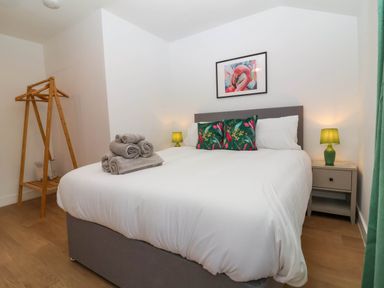 A bedroom with a bed with white sheets green pillows bedside tables with lamps and a wooden clothes stand at Woodland Roost Parkham near Bideford