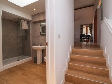 A bathroom with shower and sink next to wooden stairs leading to a room with a table and chairs at Woodland Roost Parkham near Bideford