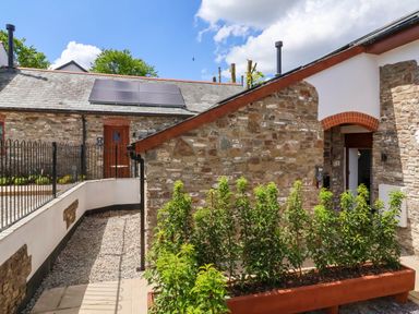 A courtyard with stone buildings and plants in a planter at Ladybird Rest in Parkham near Bideford
