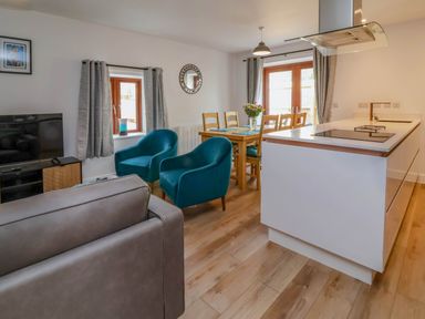 An open plan living room and kitchen with blue armchairs wooden dining table and white kitchen island at Ladybird Rest in Parkham near Bideford