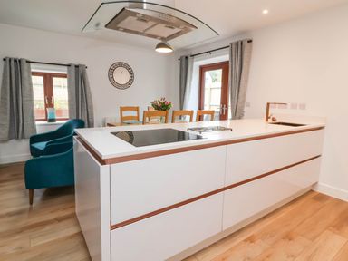A kitchen with a white island and cooktop next to a dining table with flowers and wooden chairs at Ladybird Rest in Parkham near Bideford