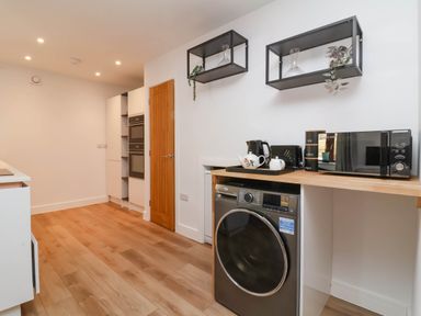 A kitchen area with wooden floor washing machine microwave kettle and oven at Ladybird Rest in Parkham near Bideford
