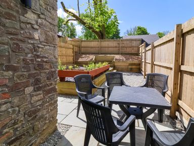 An outdoor patio area with a table and four chairs surrounded by wooden fencing and a raised garden bed at Ladybird Rest in Parkham near Bideford