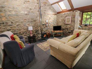 A living room with stone walls a wood stove a TV two couches and a window at The Old Stable in Pontfaen near Fishguard