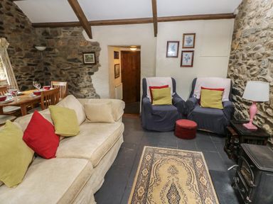 A living room with armchairs a sofa dining table and stone walls at The Old Stable in Pontfaen near Fishguard
