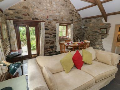 A living room with a beige sofa and dining table against stone walls at The Old Stable in Pontfaen near Fishguard