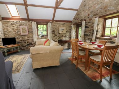 A living room with a beige sofa a wooden dining table with chairs and stone walls at The Old Stable in Pontfaen near Fishguard