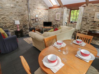 A stone wall living room with a wood stove a wooden dining table set with bowls and wine glasses at The Old Stable in Pontfaen near Fishguard