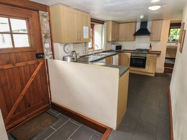 A kitchen with wooden cabinets a gas stove a microwave and a wooden door at The Old Stable in Pontfaen near Fishguard