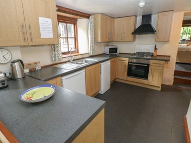 A kitchen with wooden cabinets black countertops and a gas stove at The Old Stable in Pontfaen near Fishguard