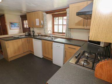 A kitchen with wooden cabinets a gas stove a dishwasher a sink and a window with curtains at The Old Stable in Pontfaen near Fishguard