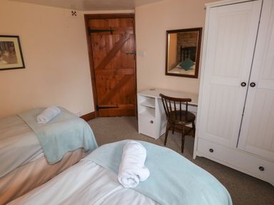 A bedroom with two single beds a wooden chair a white desk and a wardrobe at The Old Stable in Pontfaen near Fishguard